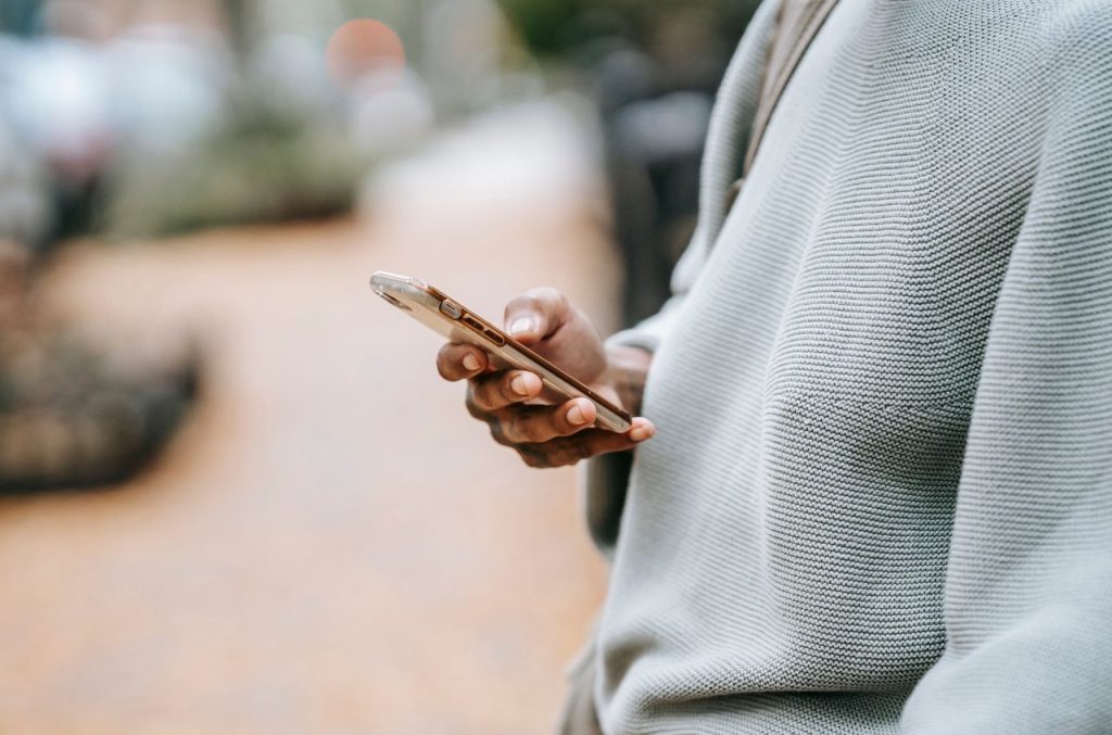 Crop unrecognizable female holding modern smartphone and messaging while standing on city street