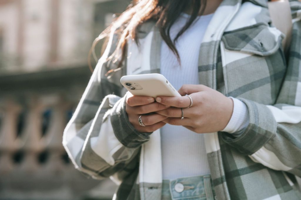 Crop faceless young woman in casual outfit text messaging on phone in city street in daytime